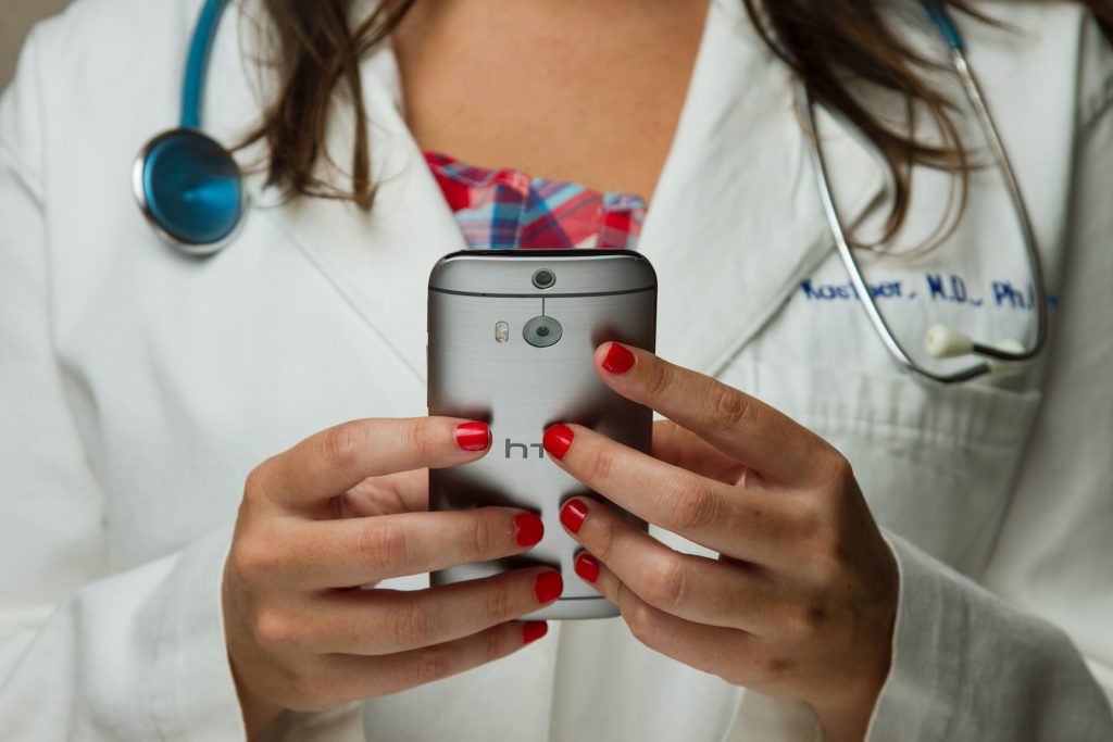 Doctor in white coat using smartphone, wearing stethoscope around neck