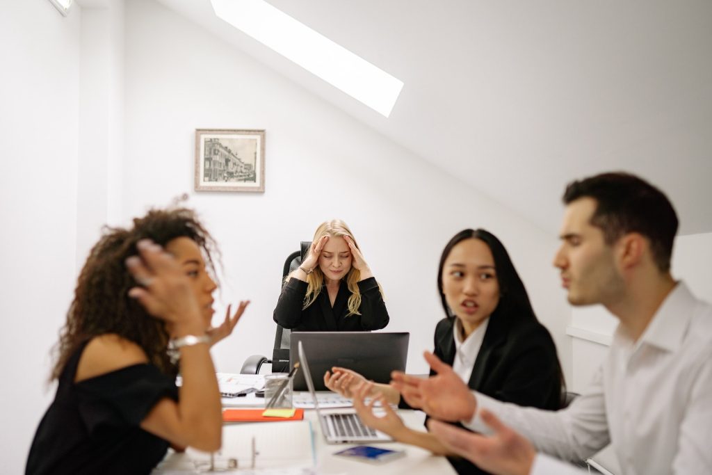 Business team in conflict with a stressed manager at a desk in a bright office setting, discussing strategies