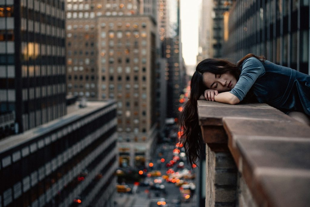 Woman resting on city rooftop edge with blurred urban skyline and traffic below